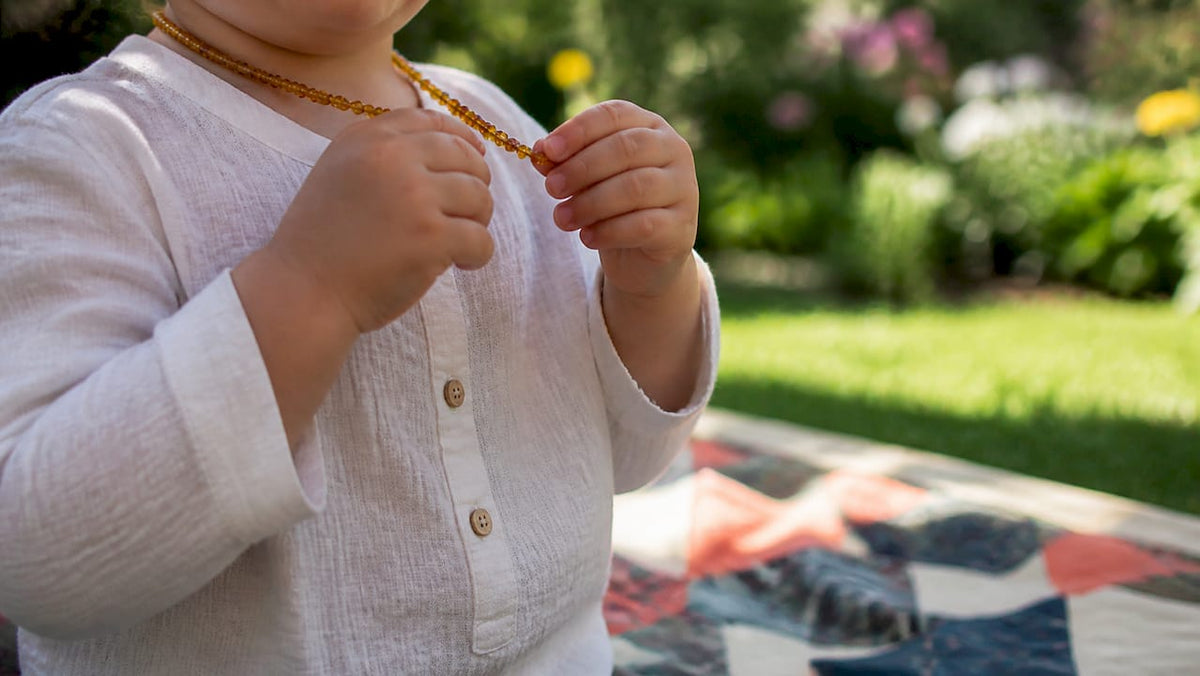 Child removing amber teething necklace outdoors